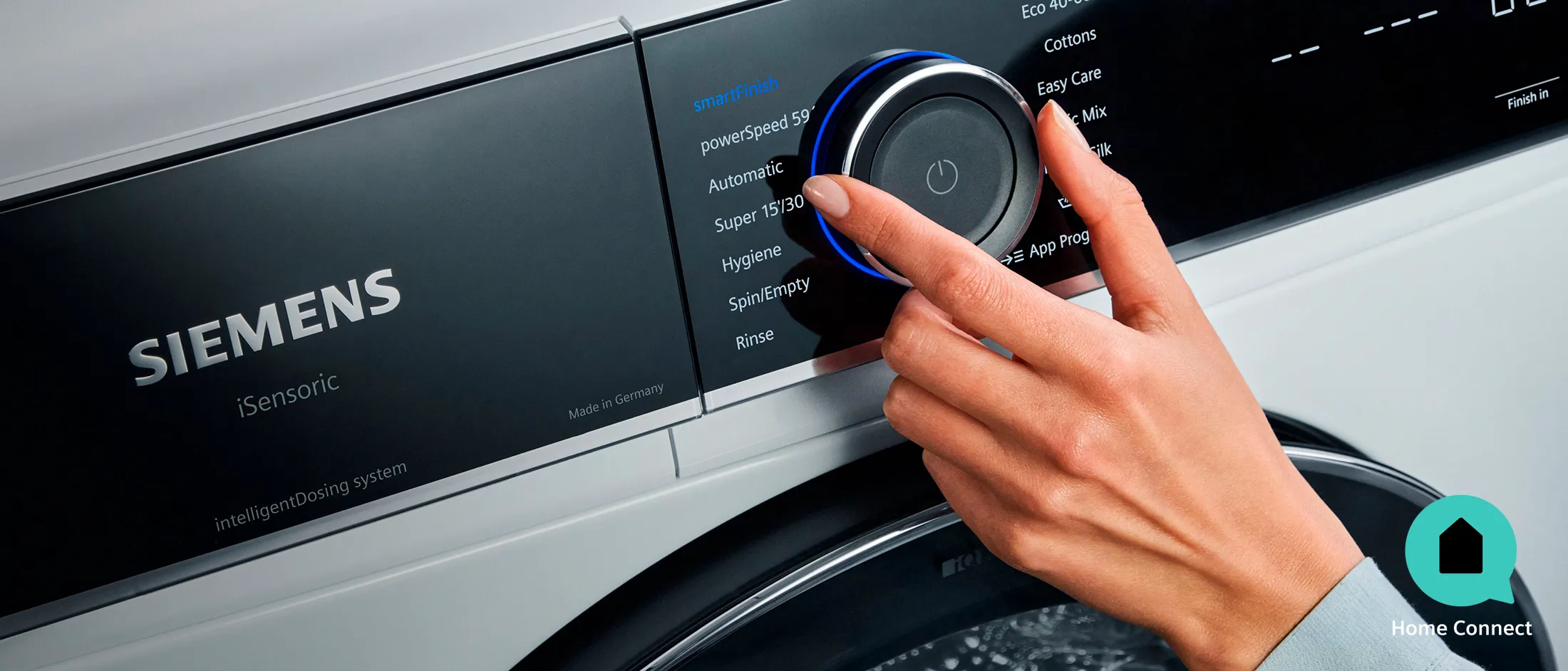 Mano che regola la manopola di controllo di una lavatrice Siemens, selezionando un programma di lavaggio sul pannello digitale dell'elettrodomestico.