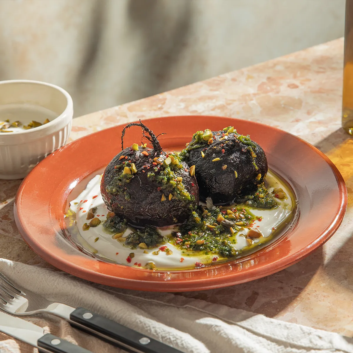 Roasted beets on a plate, garnished with herbs, accompanied by a glass of amber-colored liquid.