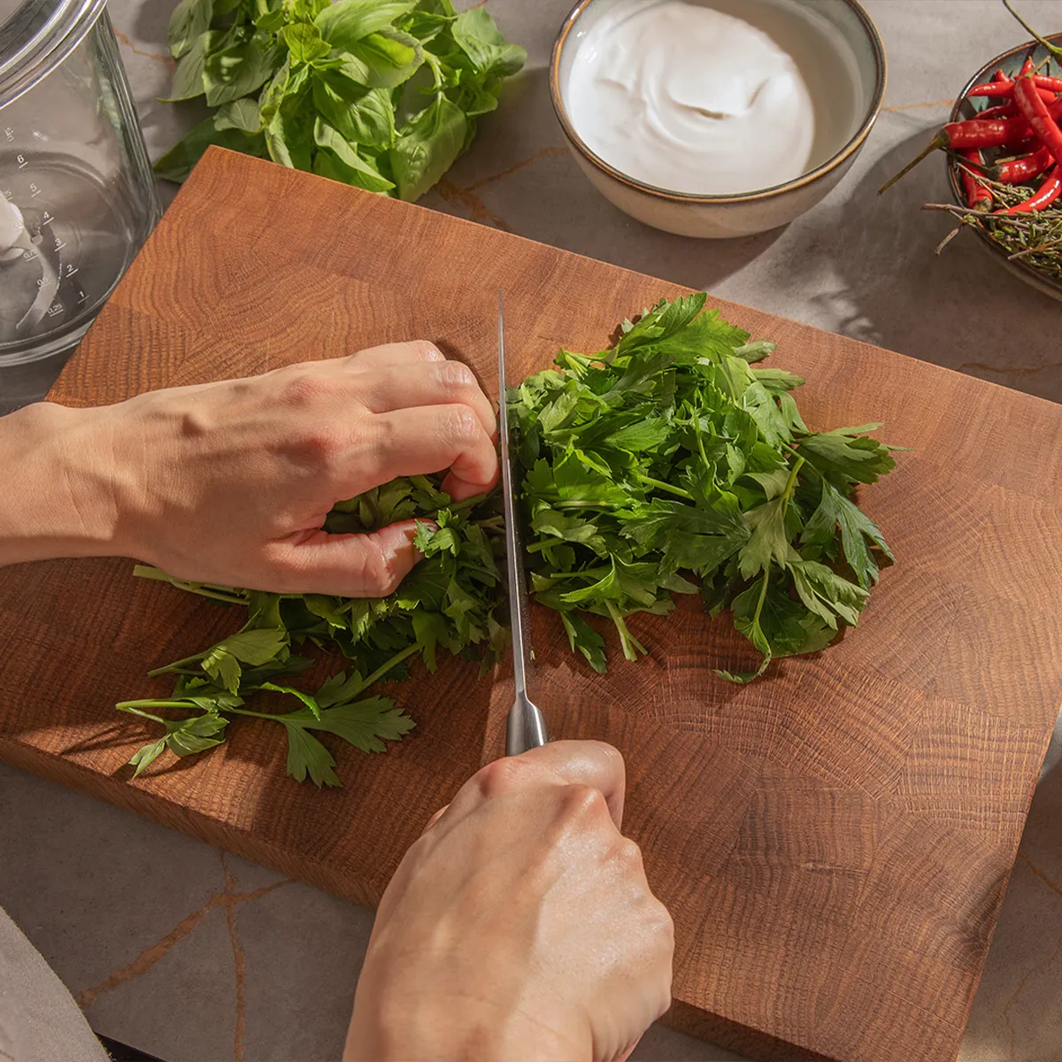 Chopping fresh parsley on a wooden board, surrounded by basil, chilies, and yogurt. Preparing a vibrant meal with Neff.