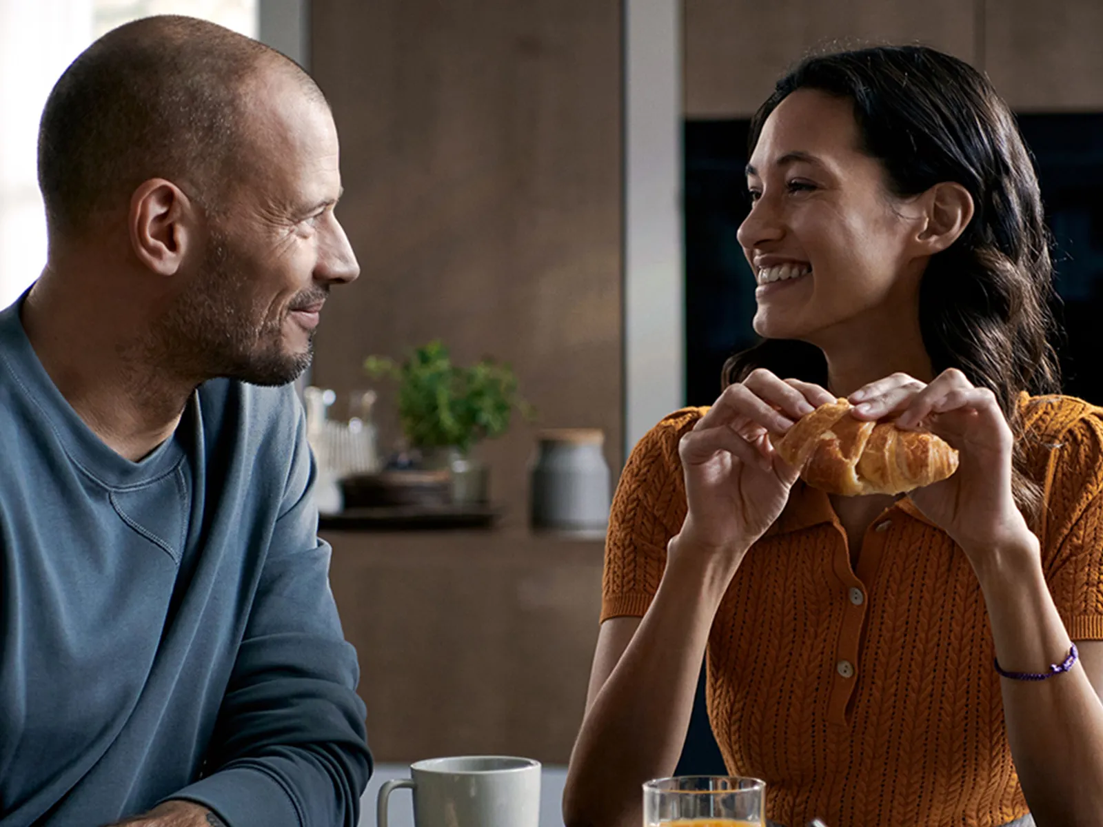 Una coppia felice fa colazione con dei croissant al tavolo della cucina.