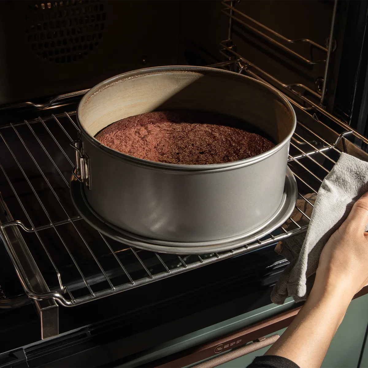 A cake bakes perfectly in a Neff oven. A hand with an oven mitt handles the pan. Effortless baking with Neff appliances.