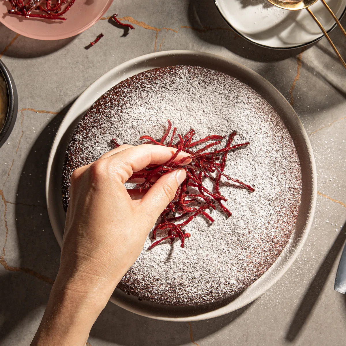 Dessert plate with powdered sugar and red garnish, hand adding final touches, dining table setting.