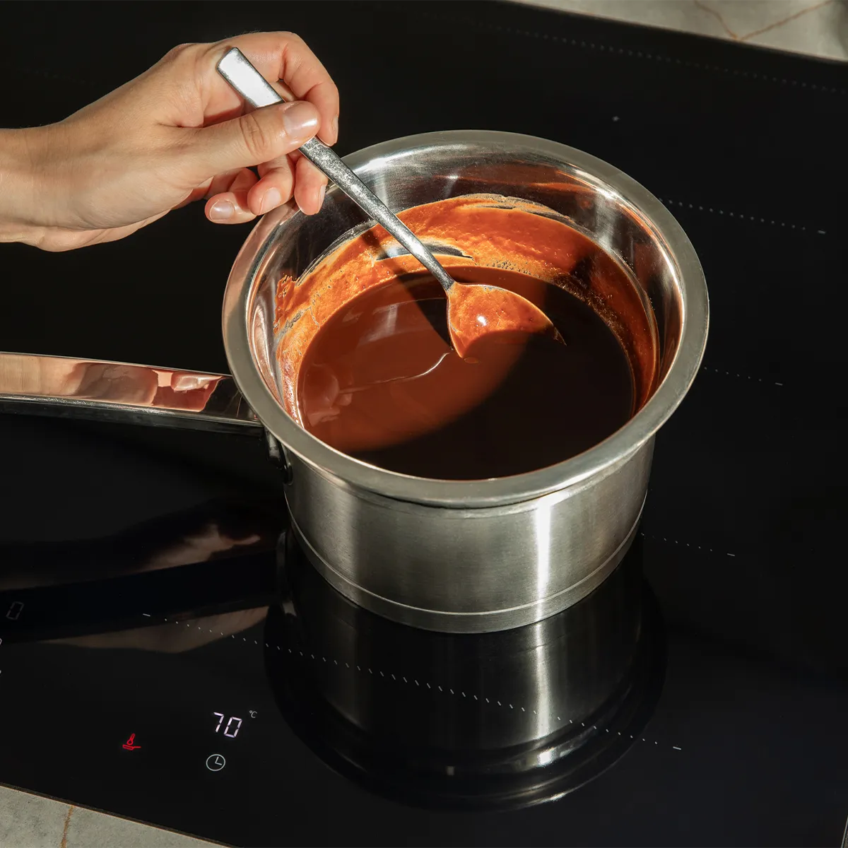 Stirring melted chocolate in a pot on a Neff induction hob, precisely at 70°C. Effortless temperature control for perfect results.