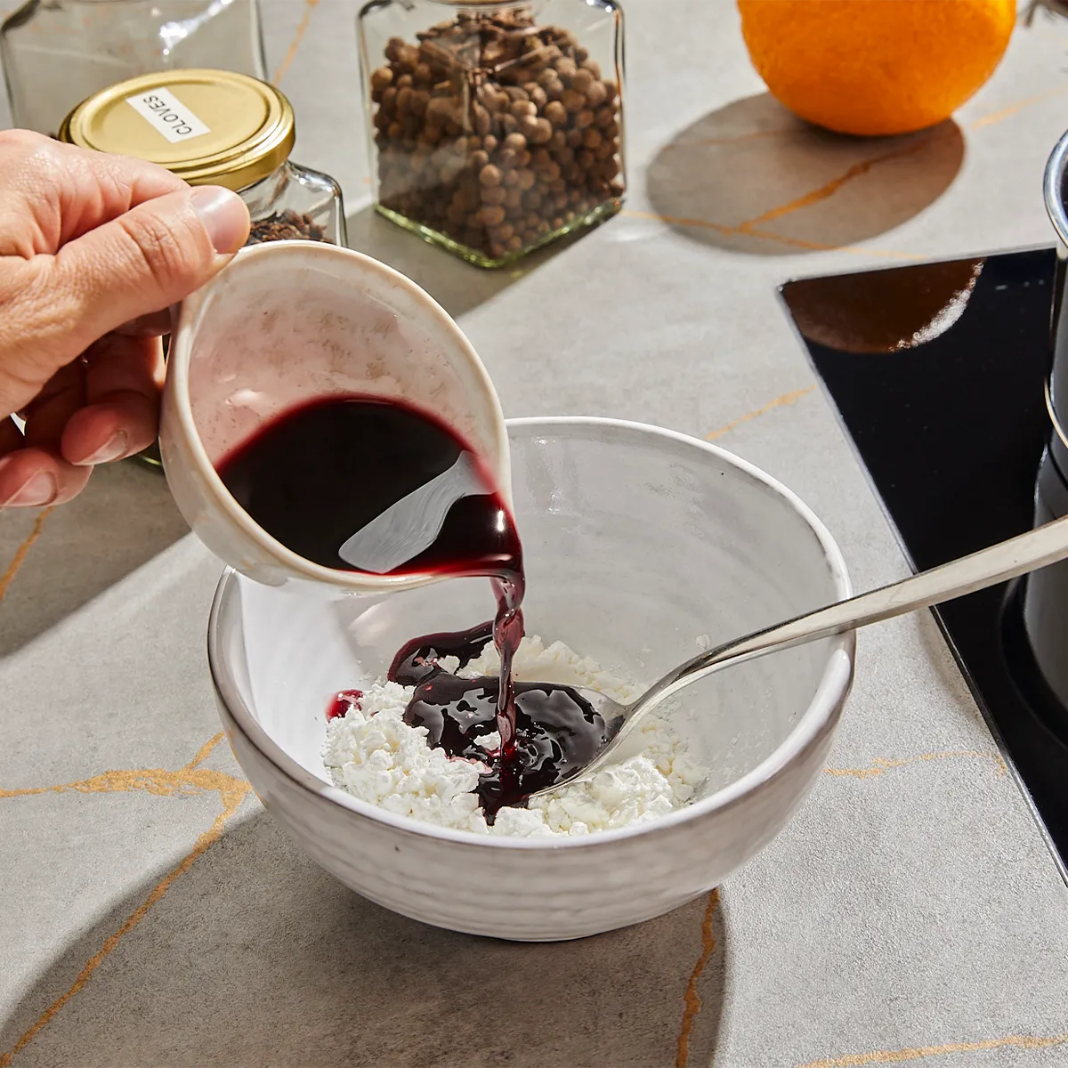 Pouring red wine into a bowl with other ingredients on a kitchen counter.