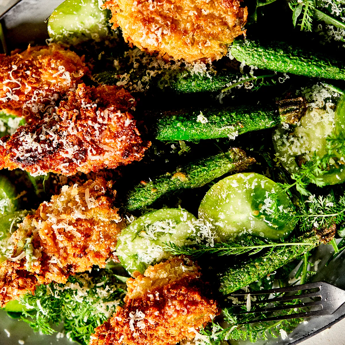Crispy fried zucchini blossoms, green veggies, and herbs, dusted with cheese. A fork is ready to serve.