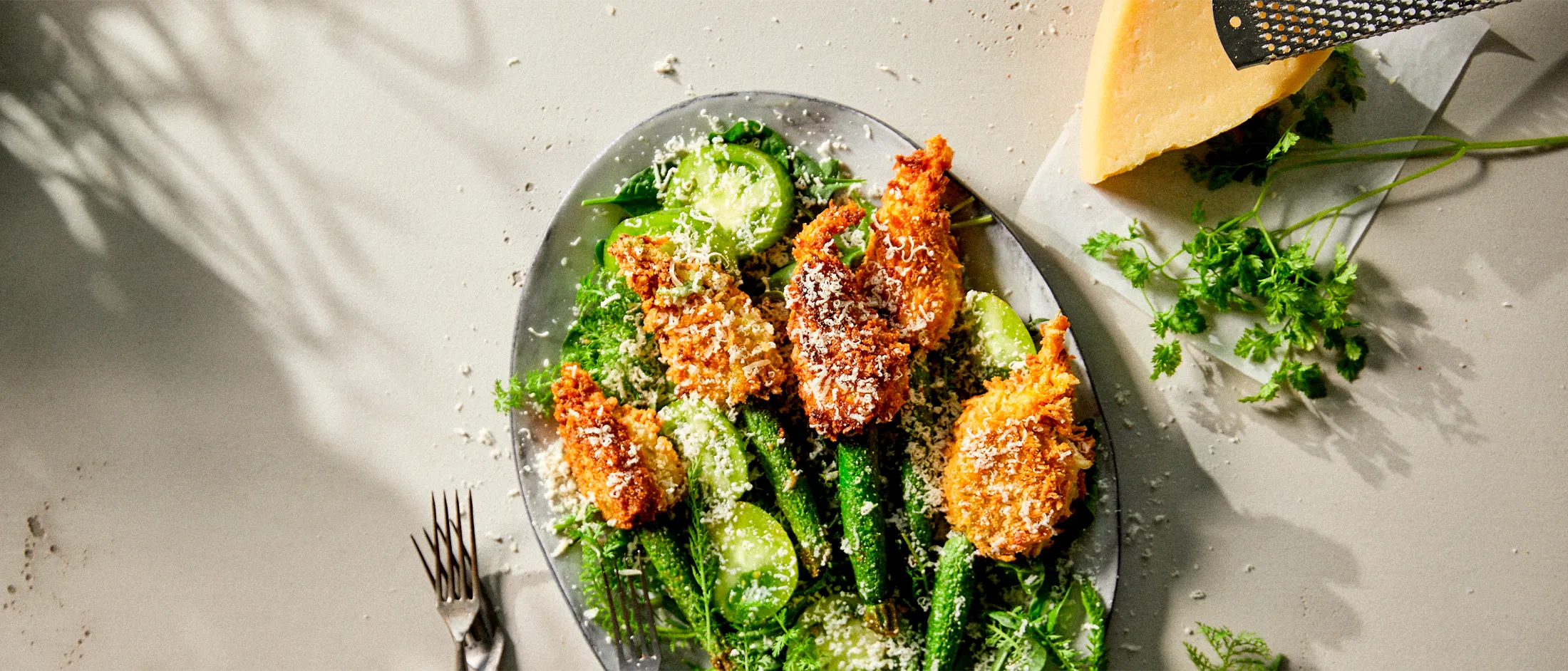 Breaded chicken, green salad, and lemon on a plate, with a fork and knife in the background.