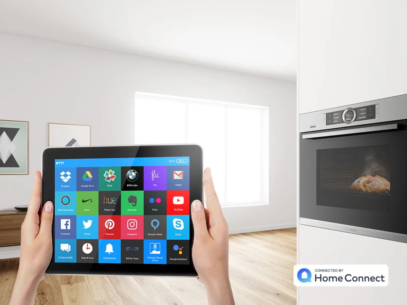 Persona che tiene in mano un tablet che mostra un'app per la casa intelligente che controlla un forno con cibo cotto all'interno in una cucina moderna.