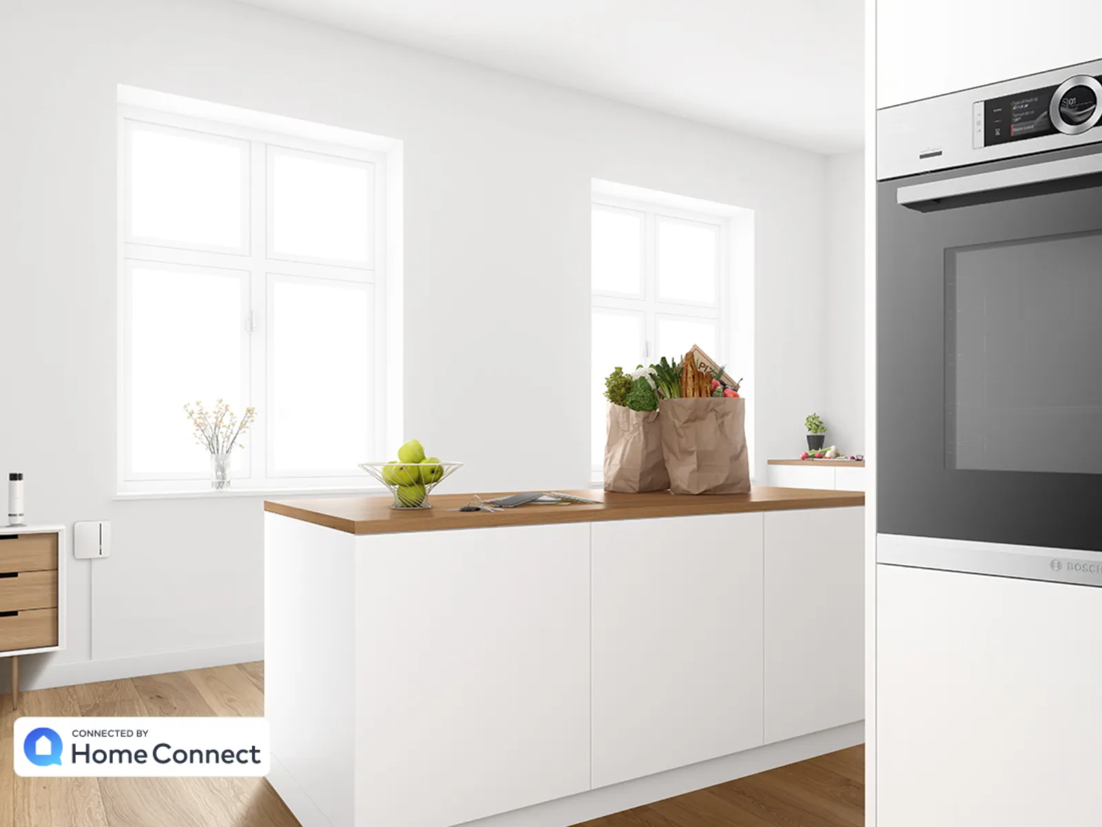 Moderna cucina bianca con pavimento in legno, un'isola con borse della spesa e fruttiera, finestre luminose e forno incorporato.