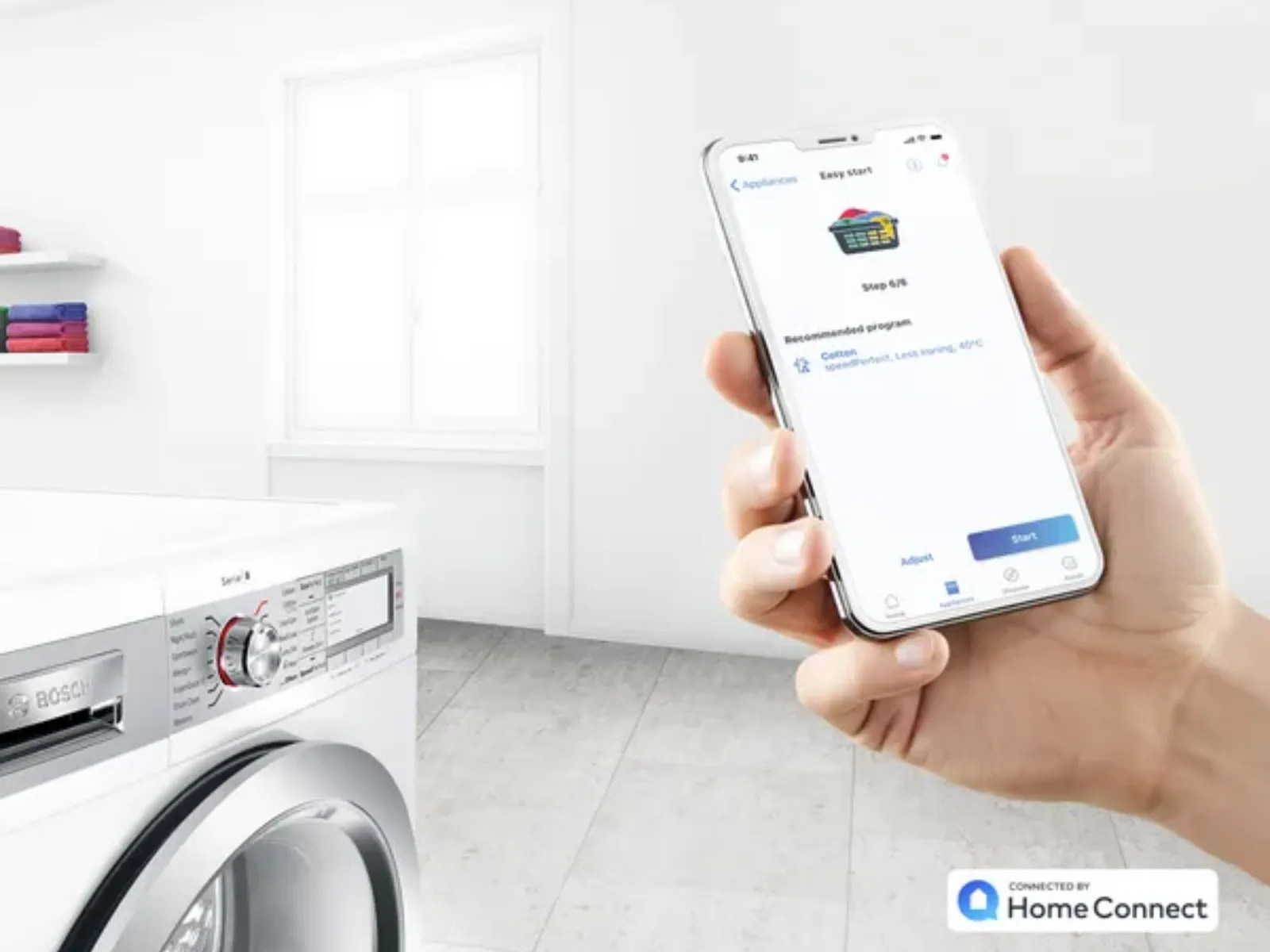 Hand holding smartphone displaying a laundry app interface near a Bosch washing machine in a bright, minimal laundry room.