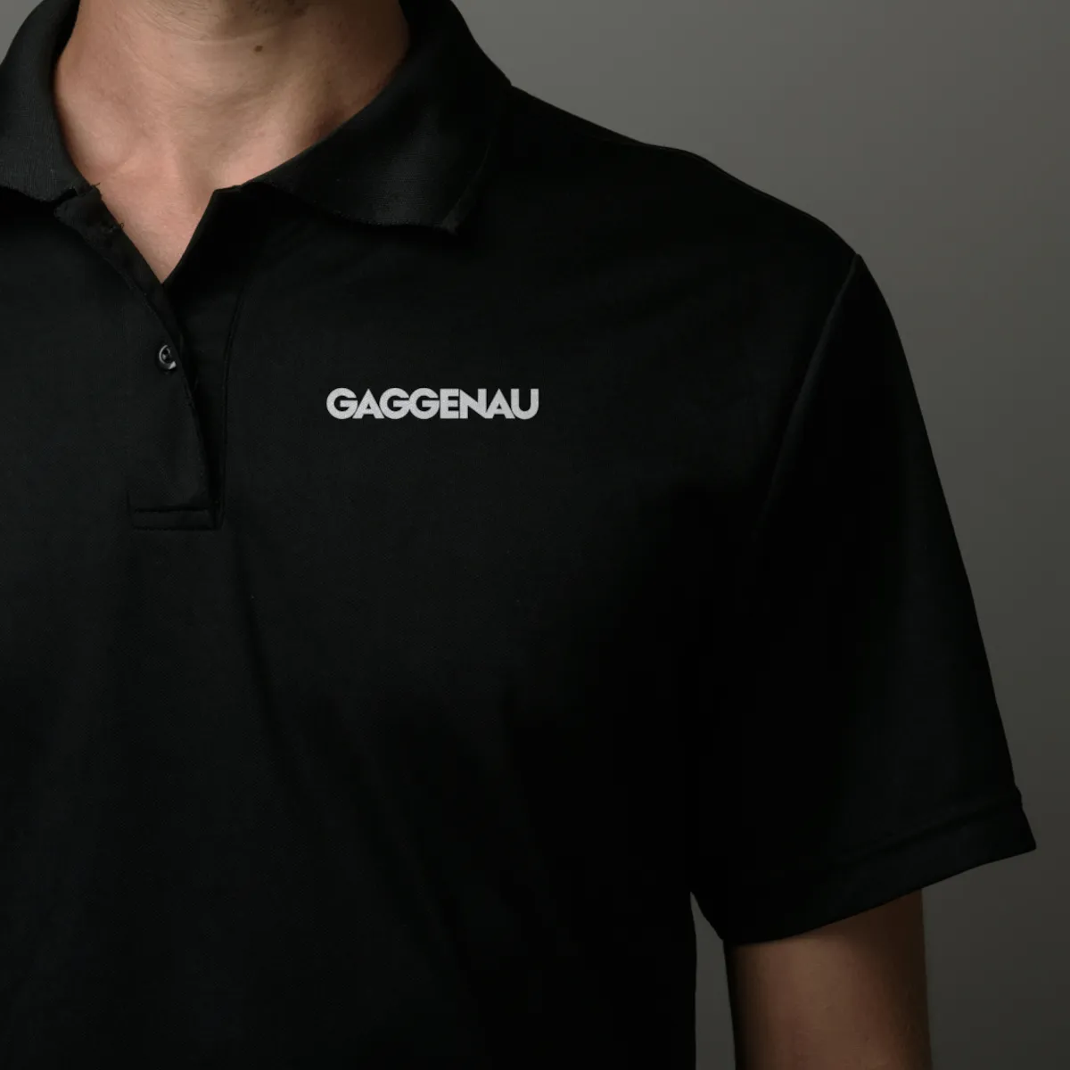 Person, die ein schwarzes Poloshirt mit dem „GAGGENAU“-Logo auf der linken Brust vor einem dunkelgrauen Hintergrund trägt.