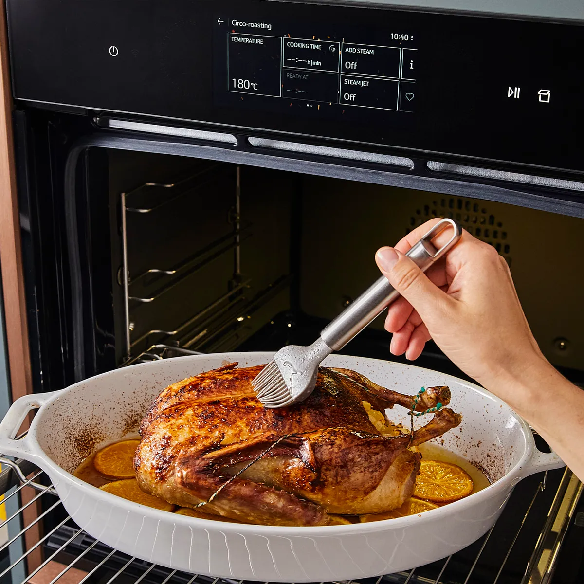 Roasted chicken in oven, hand basting with brush, kitchen appliance, cooking utensils, food preparation.