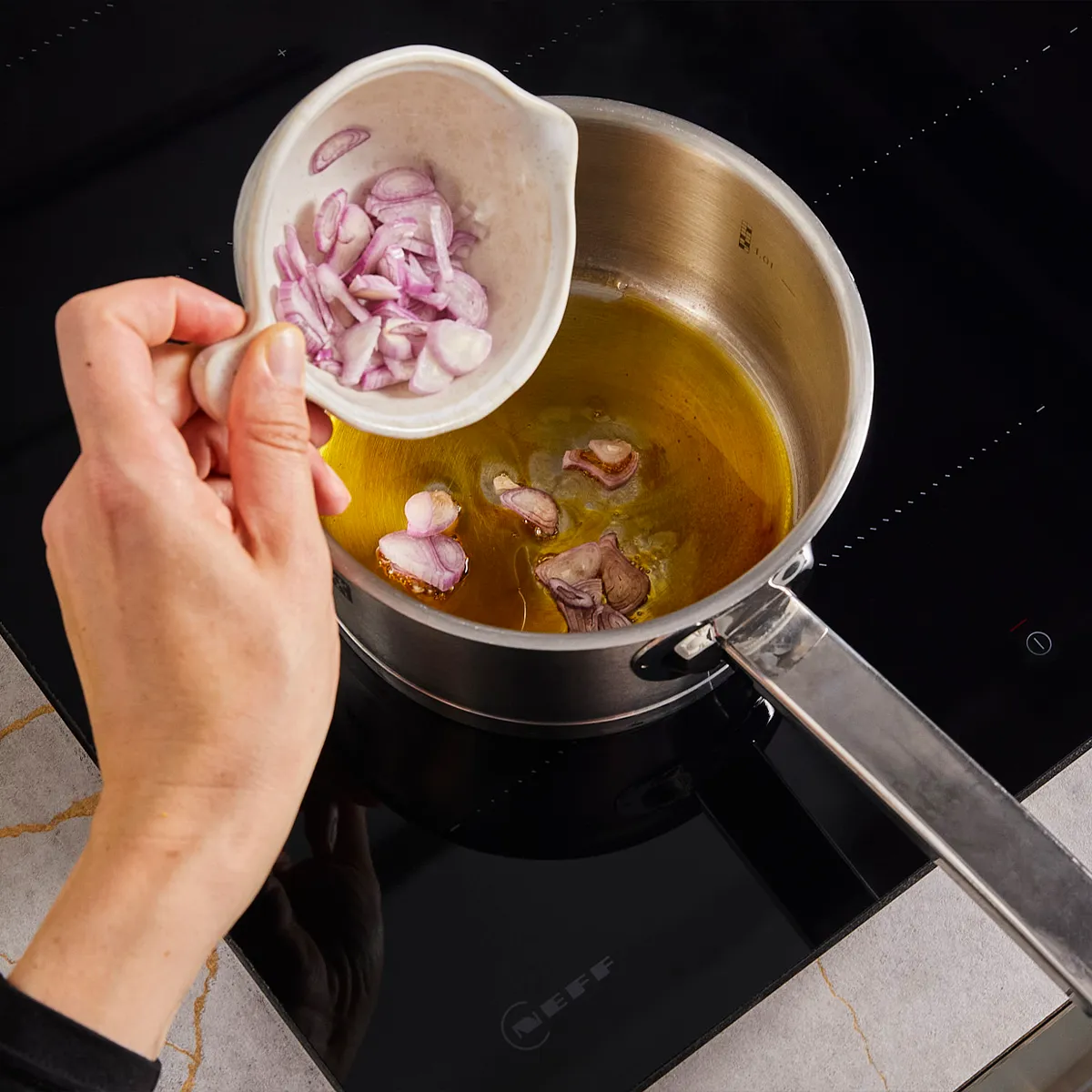 Cooking pot on stove with chopped onions, cooking utensils, and a glass of liquid on a kitchen counter.
