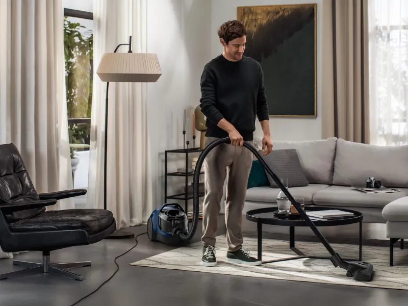 Person using a Siemens vacuum cleaner in a stylish living room, effortlessly cleaning dirt from the floor.