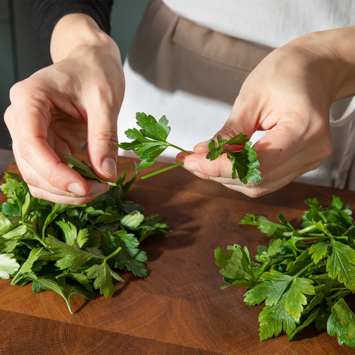 Hands chopping fresh parsley on a wooden cutting board in a kitchen setting.