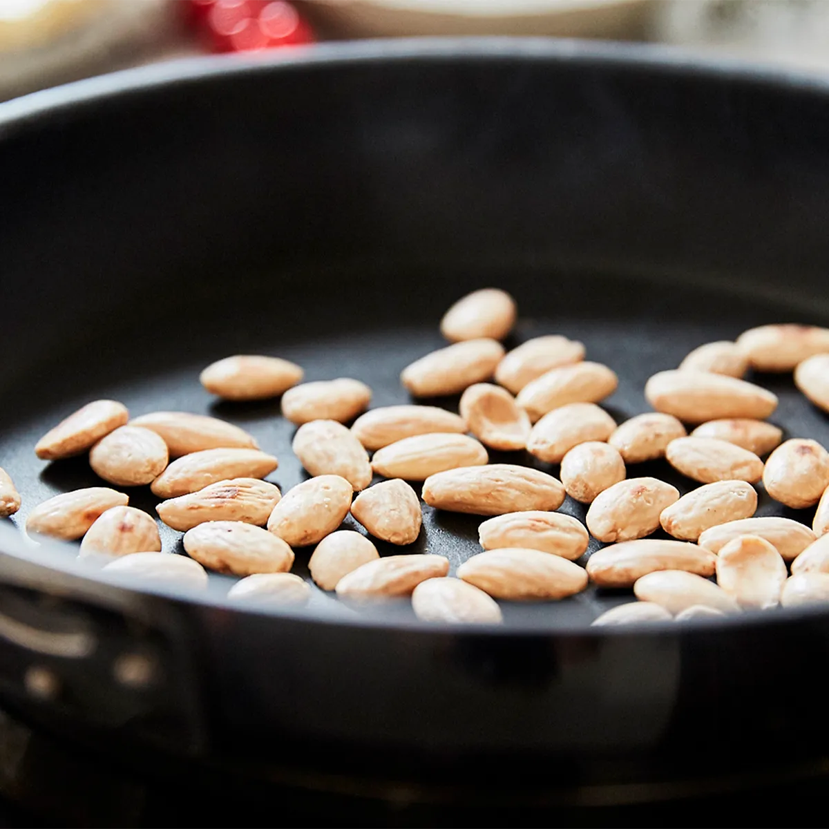 Raw almonds being toasted in a black skillet on a stovetop.
