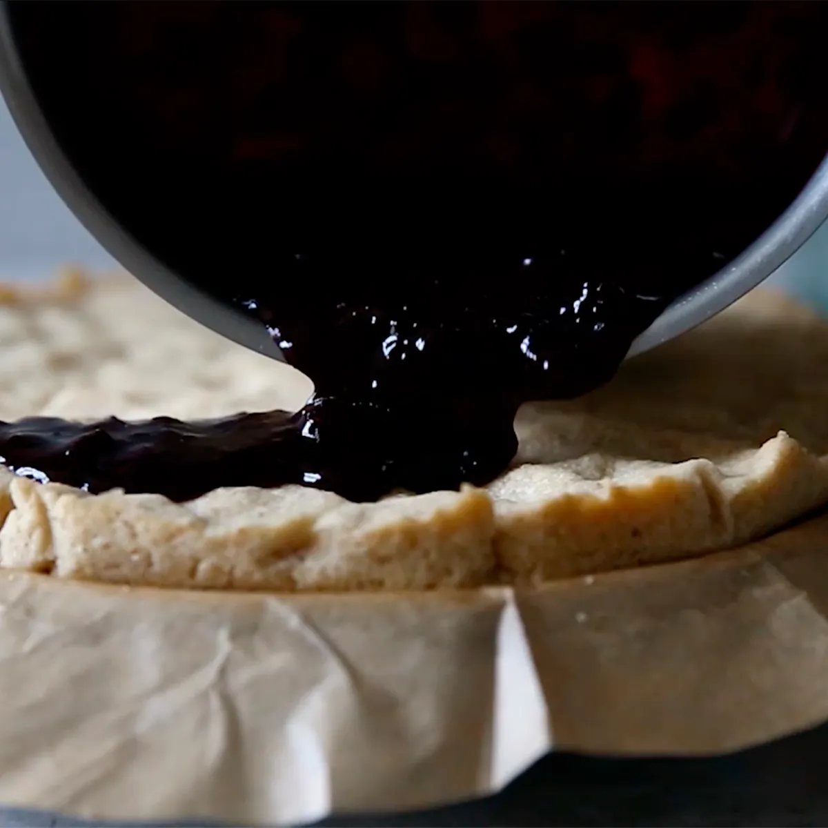 Dark berry filling poured onto a pie crust in a parchment-lined pan, ready to bake.