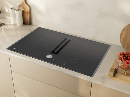 Elegantes schwarzes Induktionskochfeld mit integriertem Downdraft-Abzug, installiert auf einer hellen Küchenarbeitsplatte mit minimalistischem Dekor.