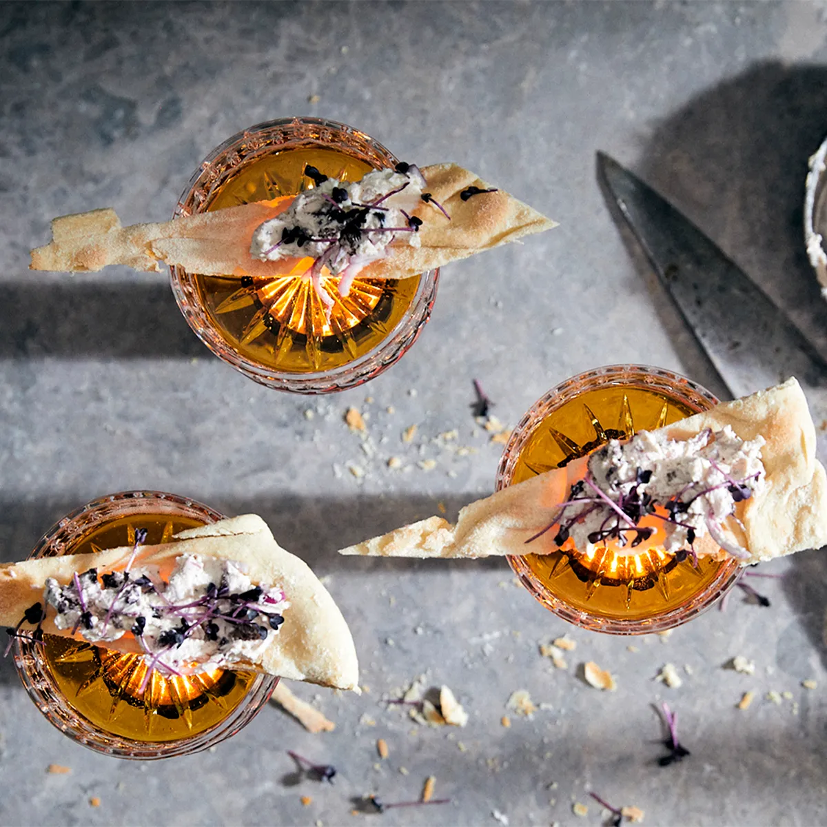 Sliced oranges with edible flowers, scattered petals, and a knife on a dark background.