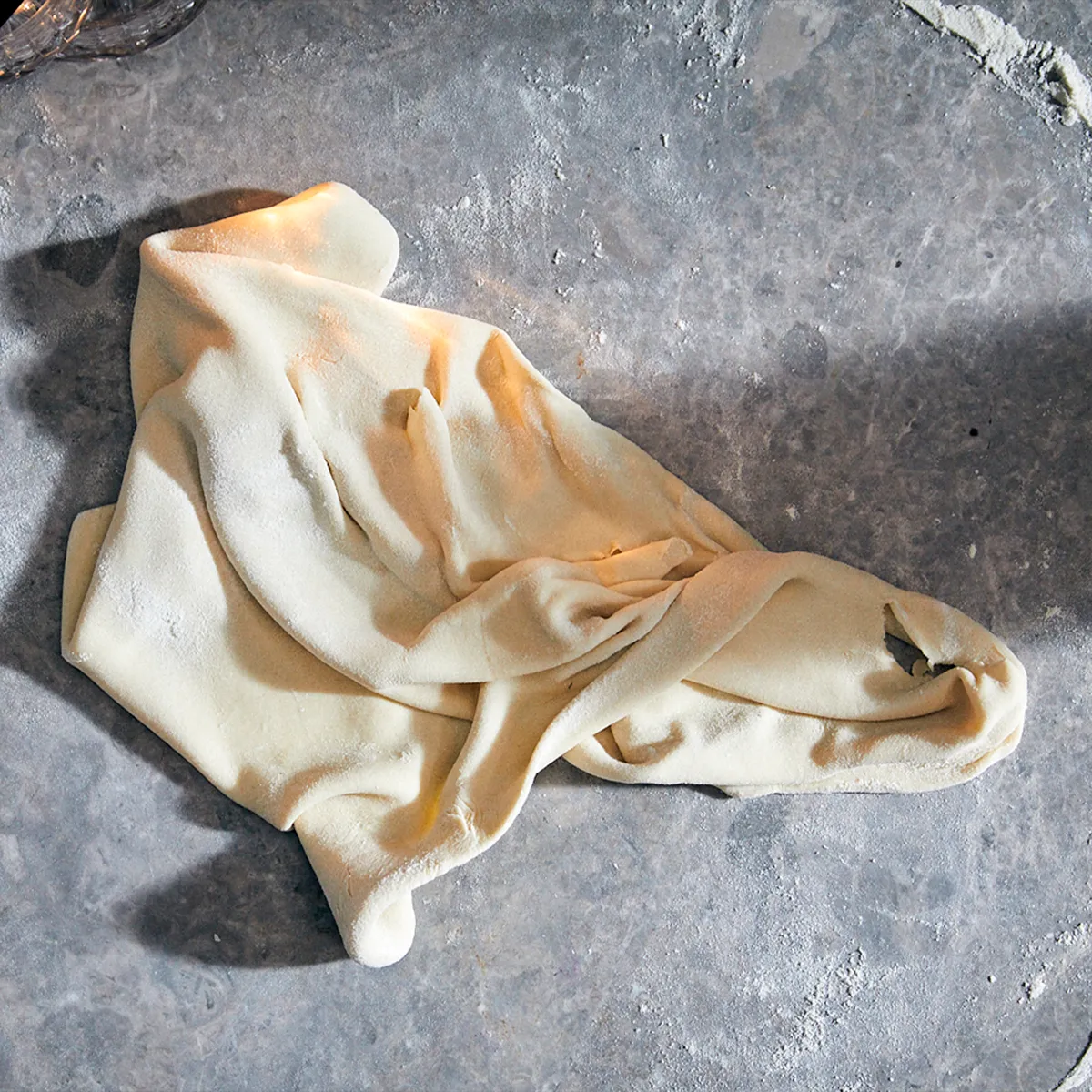 Dough lightly dusted with flour, stretched and twisted on a gray countertop.