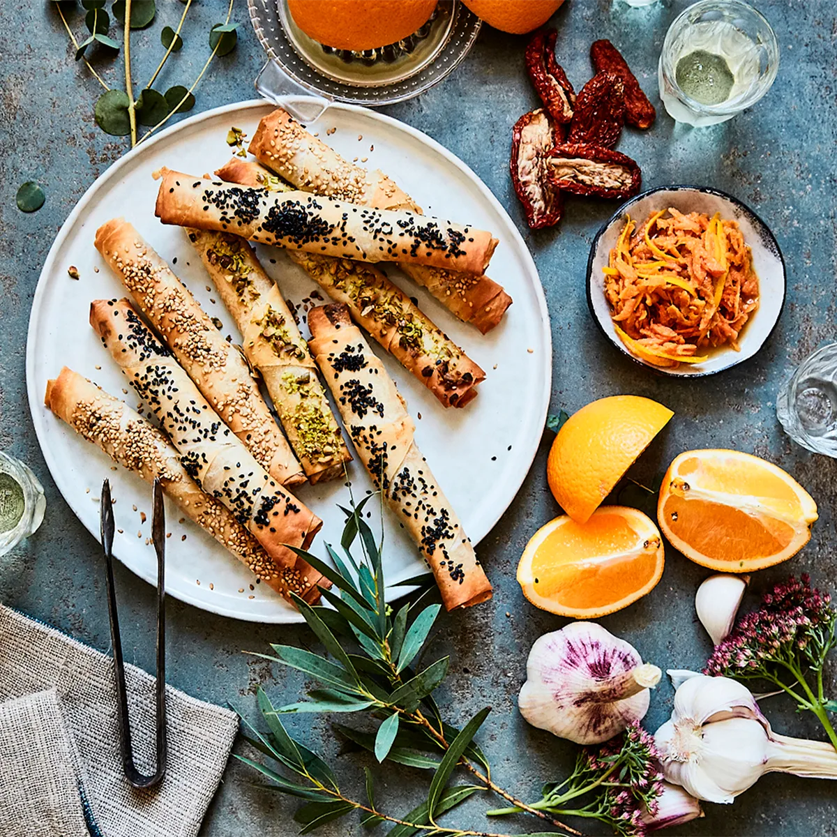 Crispy phyllo rolls with sesame & pistachio, surrounded by fresh oranges, garlic, and herbs. A delightful Neff appetizer.