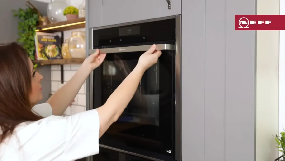 Woman installing a built-in oven into modern gray kitchen cabinetry in a bright, organized kitchen space.