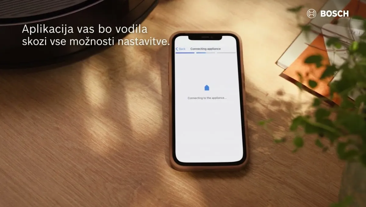 Pametni telefon na leseni mizi, na katerem je prikazan zaslon »Povezovanje naprave«, z logotipom Bosch in besedilom v slovenščini o navodilih za uporabo aplikacije.