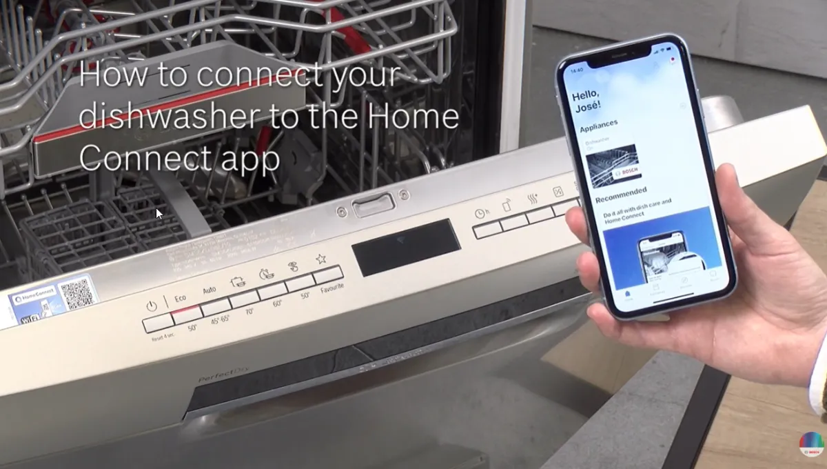 Hand holding smartphone displaying Home Connect app next to an open dishwasher with control panel visible.