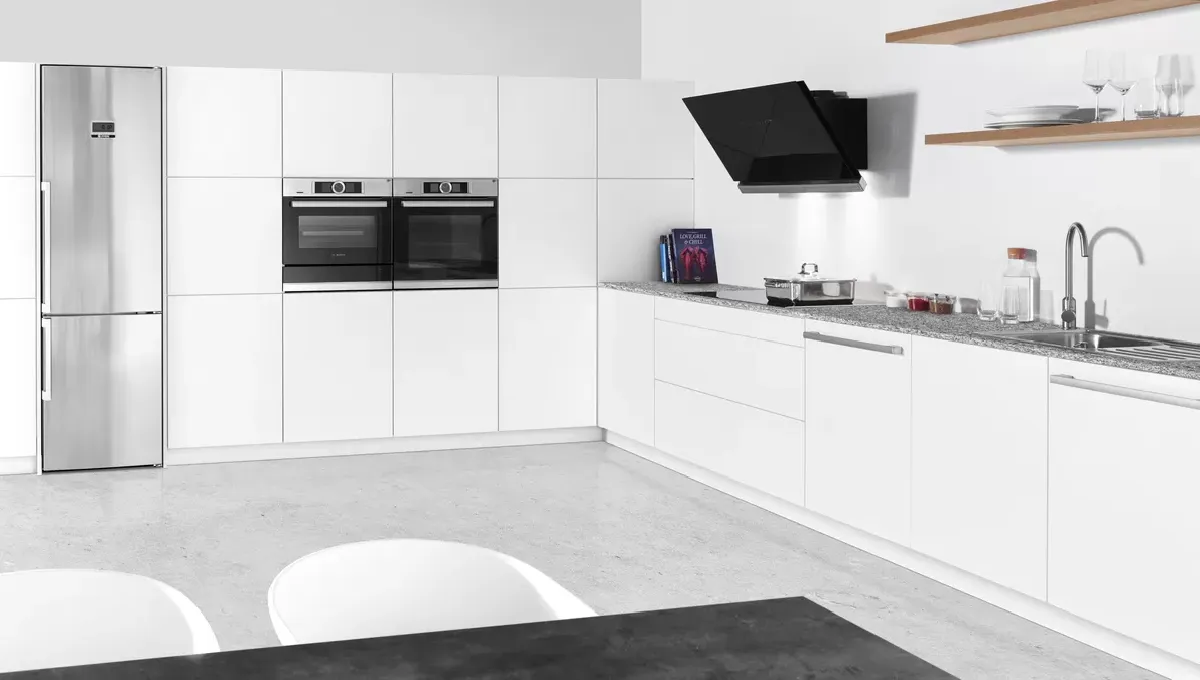 Moderne køkken med hvide skabe, stål køleskab og to ovne, samt en elegant grå bordplade.
