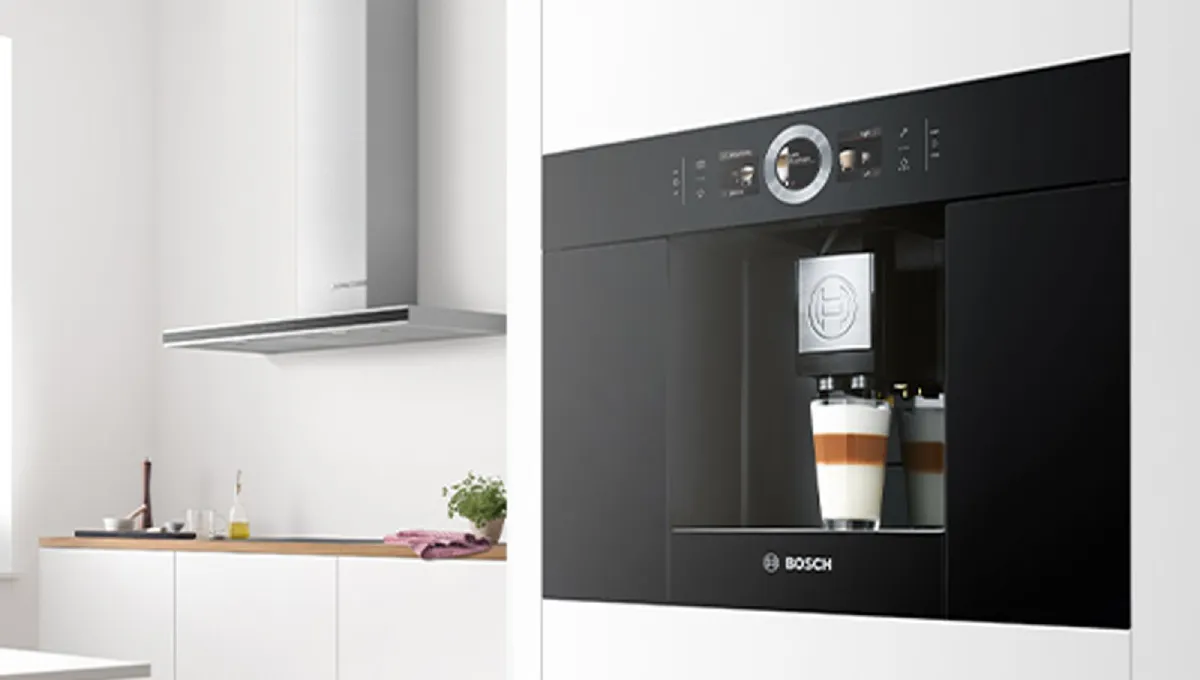 Bosch svart kaffemaskin integrerad i ett vitt kök, en kaffe latte färdiggjord i kaffemaskinen.