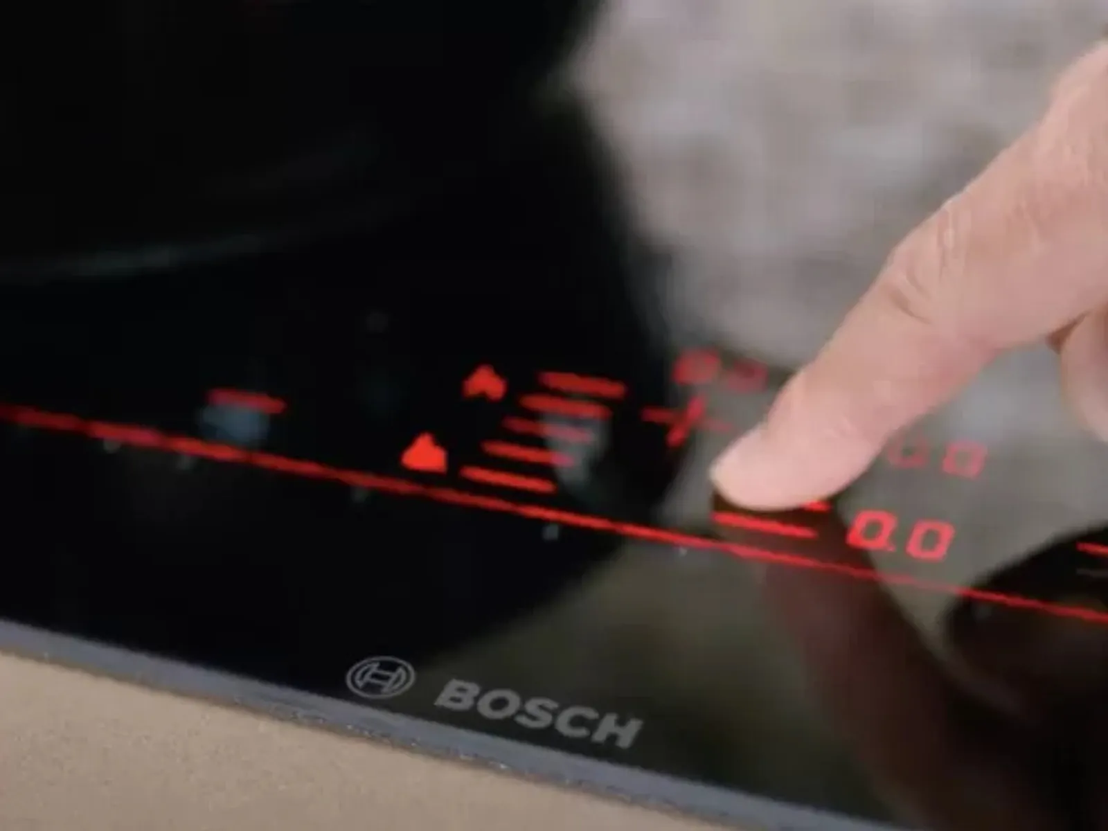 Finger adjusting the red digital touch controls on a black Bosch induction cooktop.