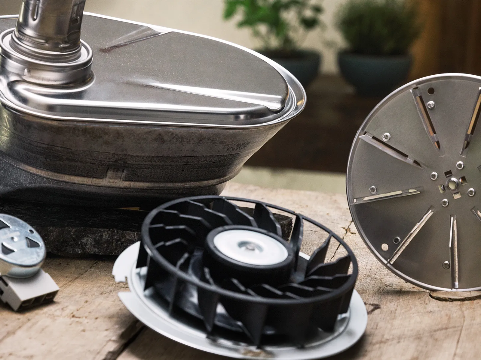 Assorted food-processor attachments on a wooden surface: stainless-steel bowl with lid, round slicing disc, plastic blade hub, and other components.
