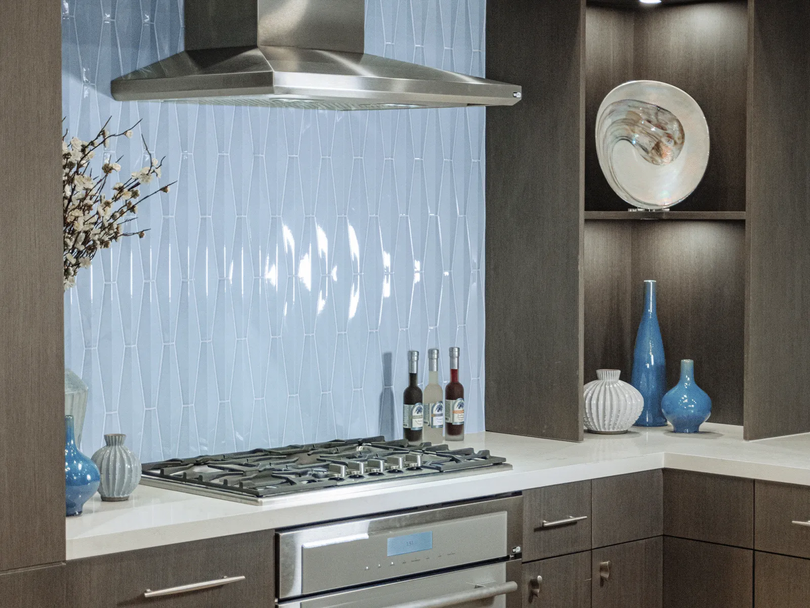 Modern kitchen with stainless steel stove, blue textured backsplash, dark wood cabinets, and decorative vases on shelves and countertop.