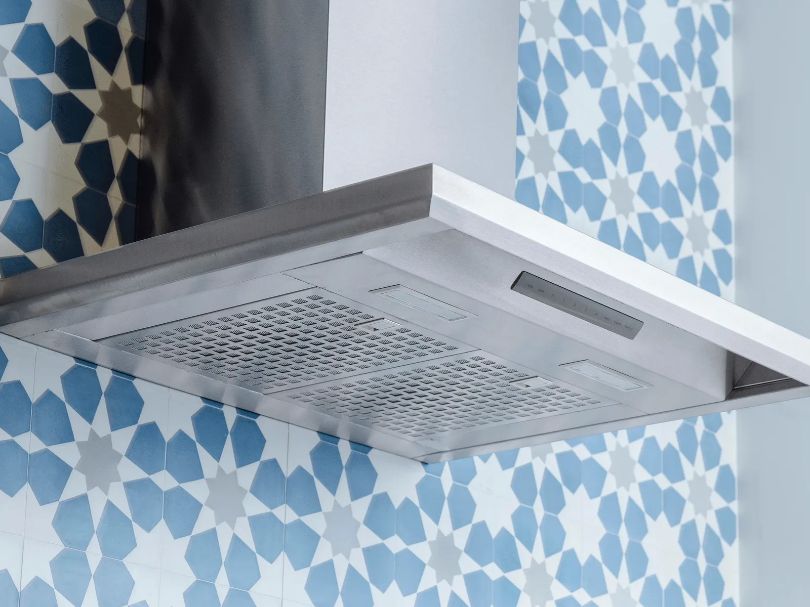 Stainless steel kitchen range hood mounted against a wall with blue and white patterned tiles.