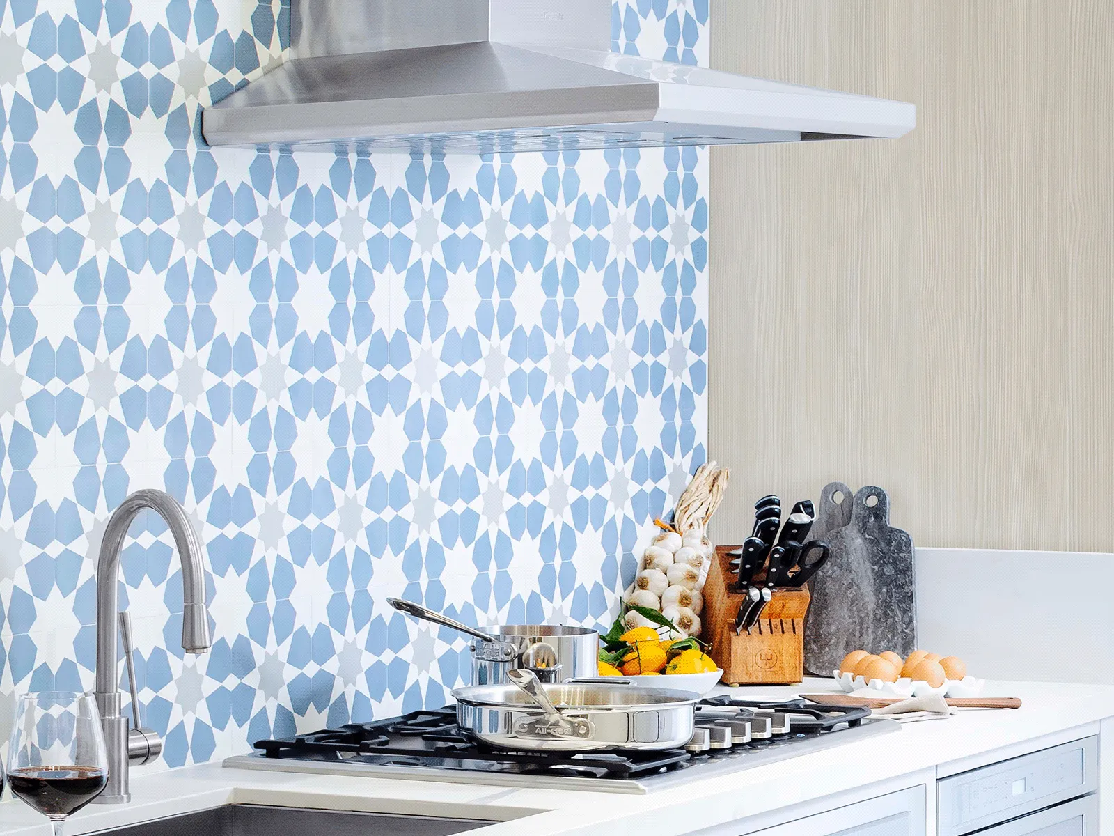 Modern kitchen countertop with a stainless steel stove, saucepan, knife set, and blue patterned tile backsplash.