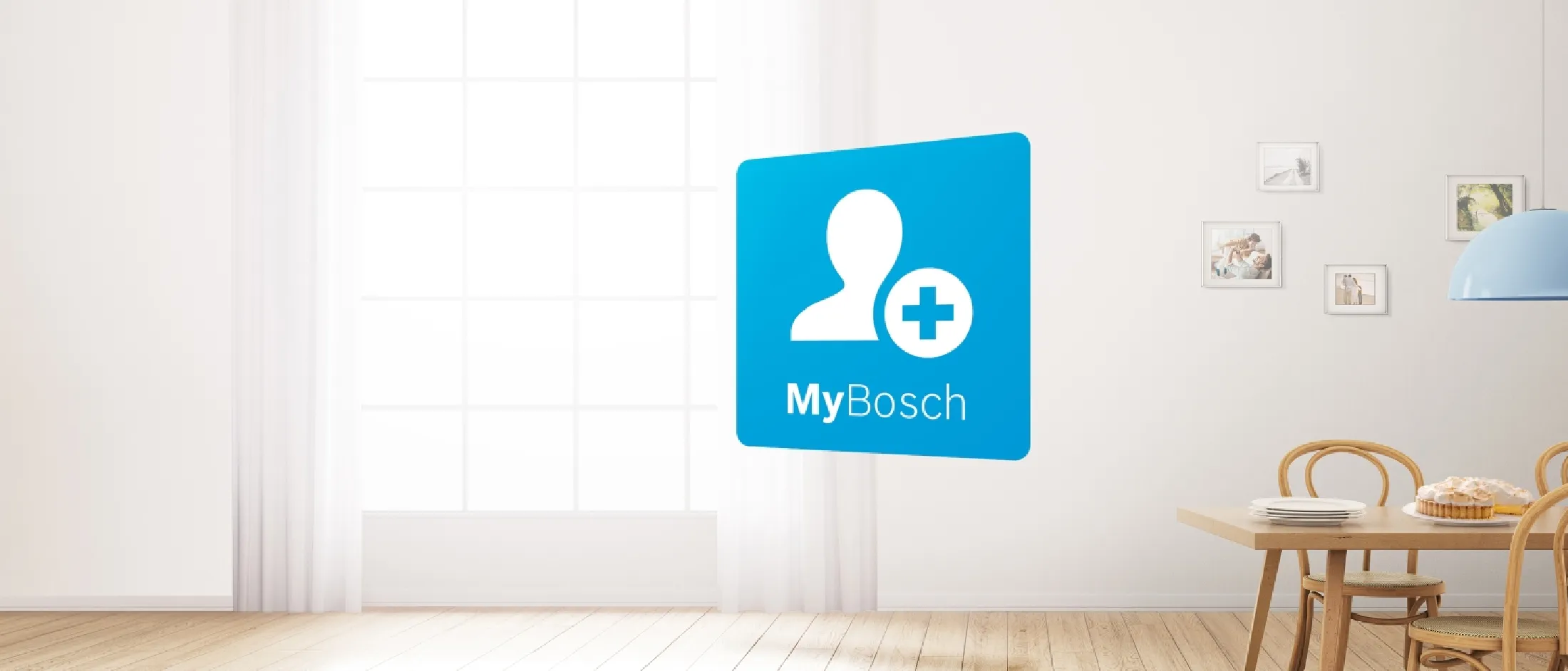 Minimālistiska ēdamistaba, kurā ir koka krēsli, galds, klāts ar šķīvjiem un kūku, gaišs logs un uz sienas projicēts MyBosch lietotnes logotips.