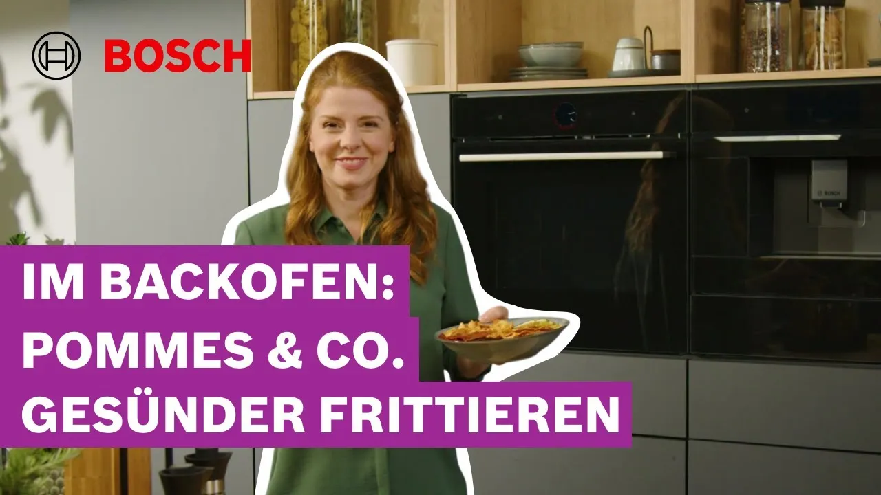 Eine lächelnde Frau hält einen Teller Pommes frites in einer modernen Küche mit Backöfen. Text: „IM BACKOFEN: POMMES & CO. GESÜNDER FRITTIEREN“.