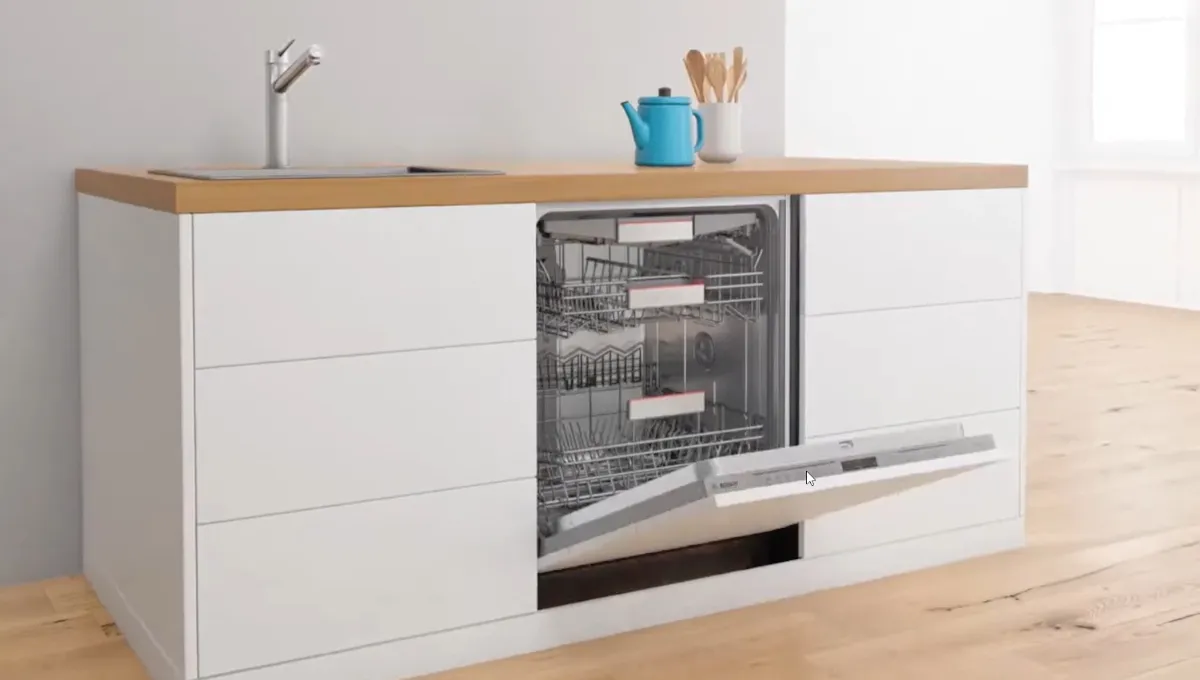 Öppen diskmaskin inbyggd i en modern vit köksinredning med bänkskiva i trä och en blå vattenkokare på bänkskivan.