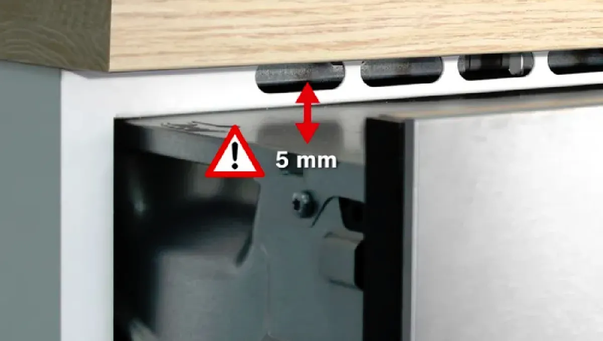 Trä skrivbord med metallram, varningsskylt som anger 5 mm gap och flera portar eller kontakter synliga.