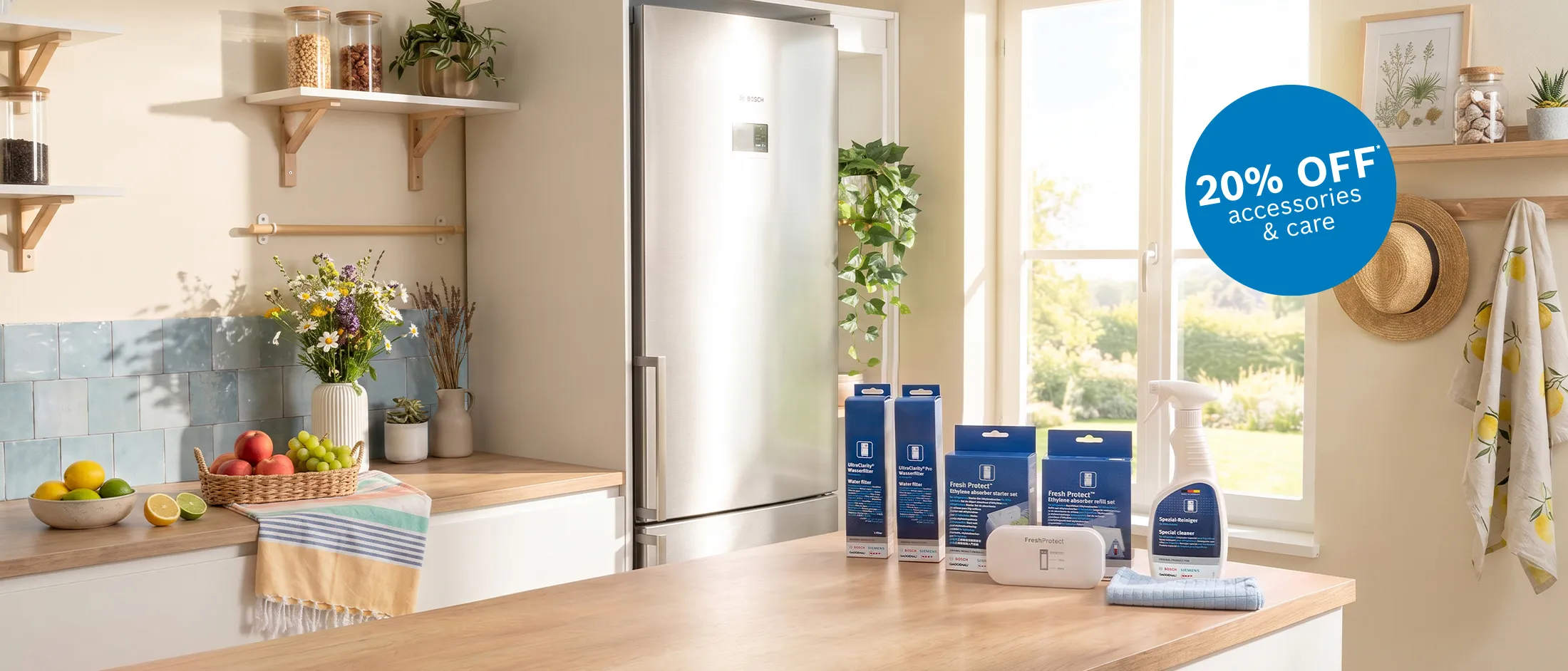 Bright, modern kitchen scene with a wooden countertop and stainless fridge; a basket of fruit and a vase of flowers sit left, while several blue-packaged appliance accessories and care products are displayed center-right. A blue circular badge in the window area states 20% OFF accessories & care.