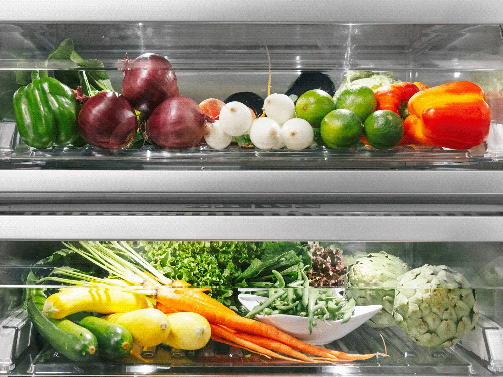 Open refrigerator with a white cake, fresh strawberries, a Caprese salad, apples in a basket, a blue pot, and leafy greens.