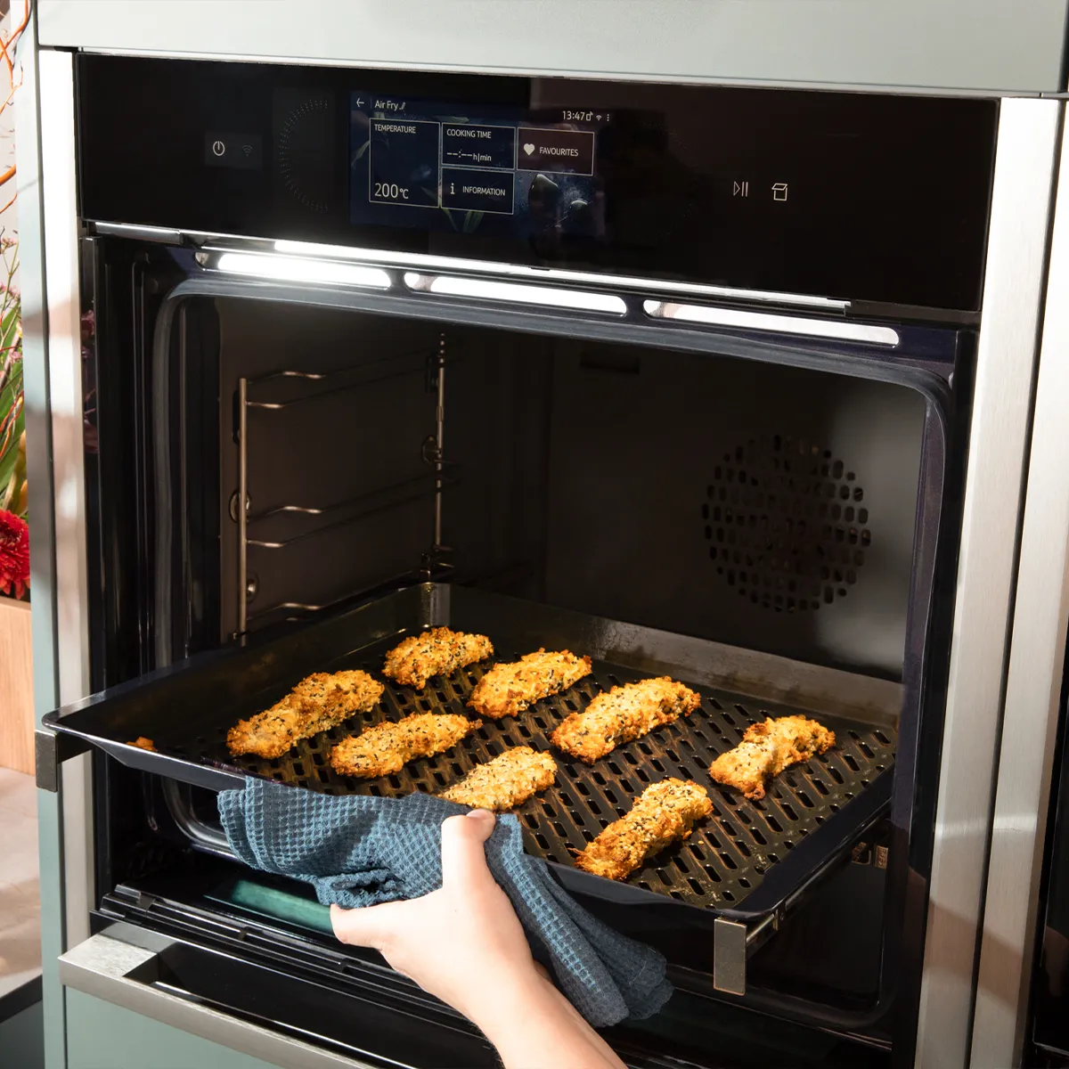 Person removing a tray of baked chicken from an oven with an air fry setting at 200 degrees.
