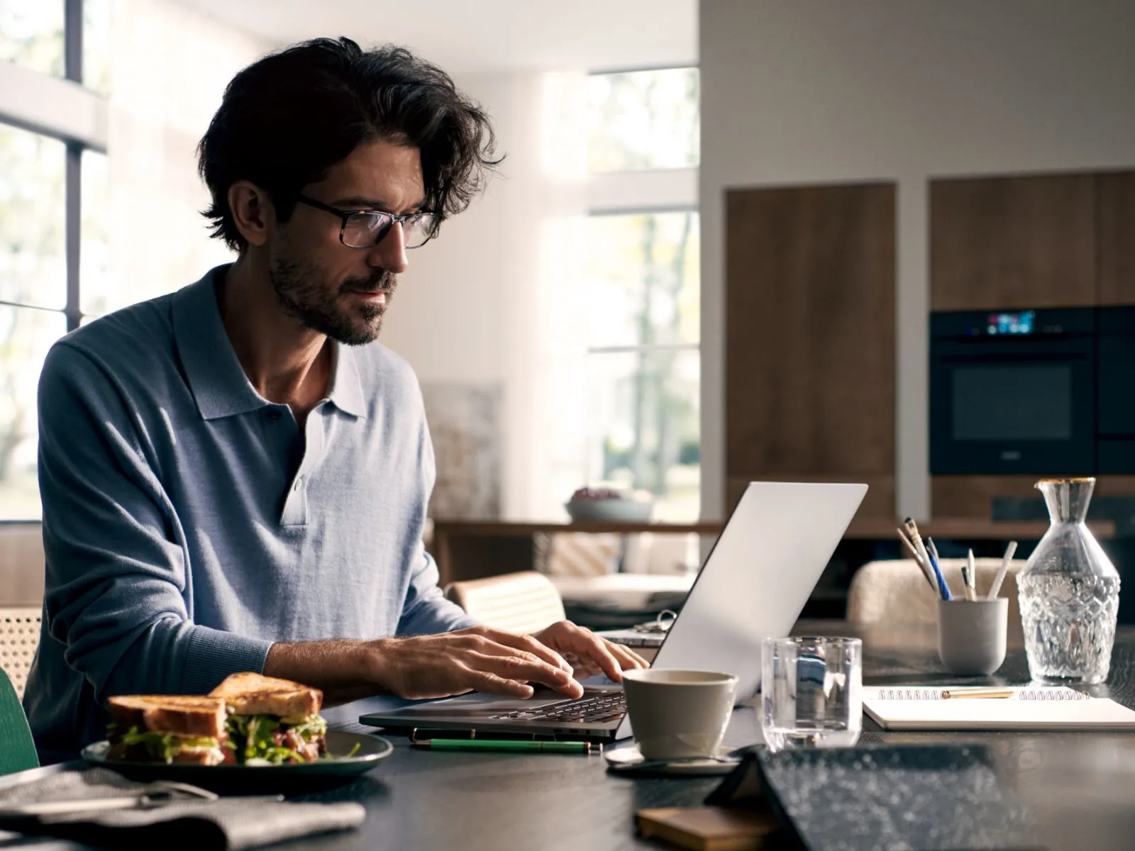 Der Mann arbeitet an Laptop, während er Sandwich in der modernen Küche isst.