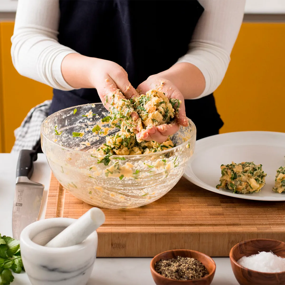 Person preparing a mixture in a glass bowl on a cutting board, with spices and herbs nearby.