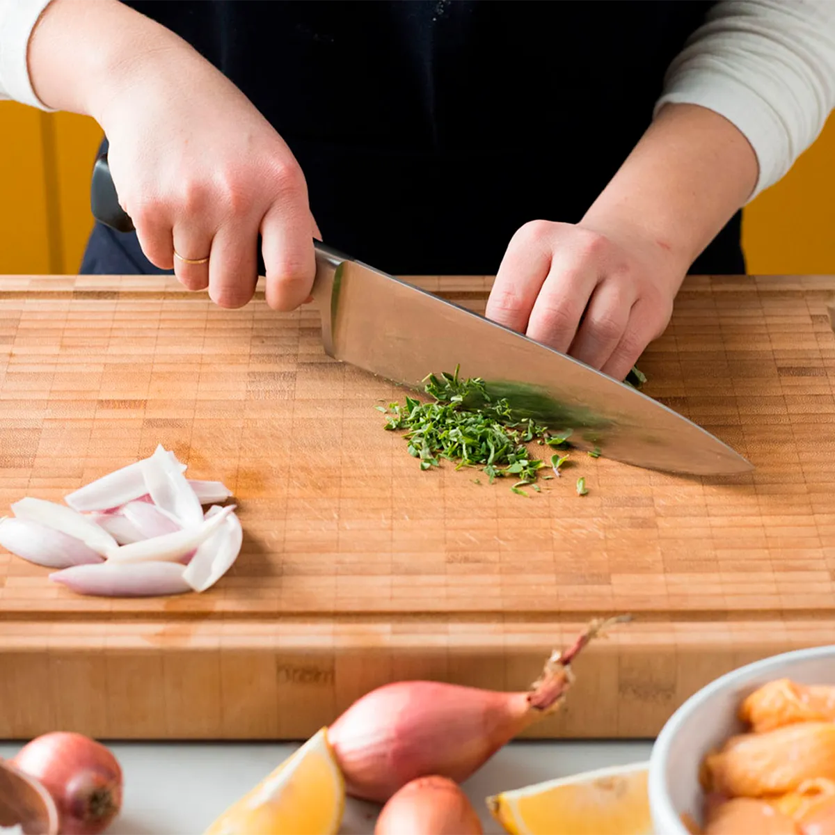 Person chopping herbs on a wooden cutting board with sliced onions and lemons nearby.
