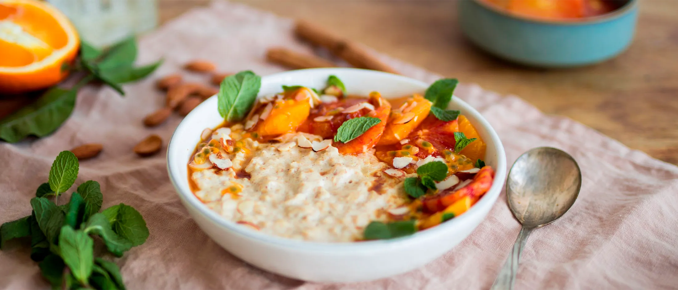 A bowl of oatmeal topped with fresh fruit, mint leaves, and almonds with a spoon beside.