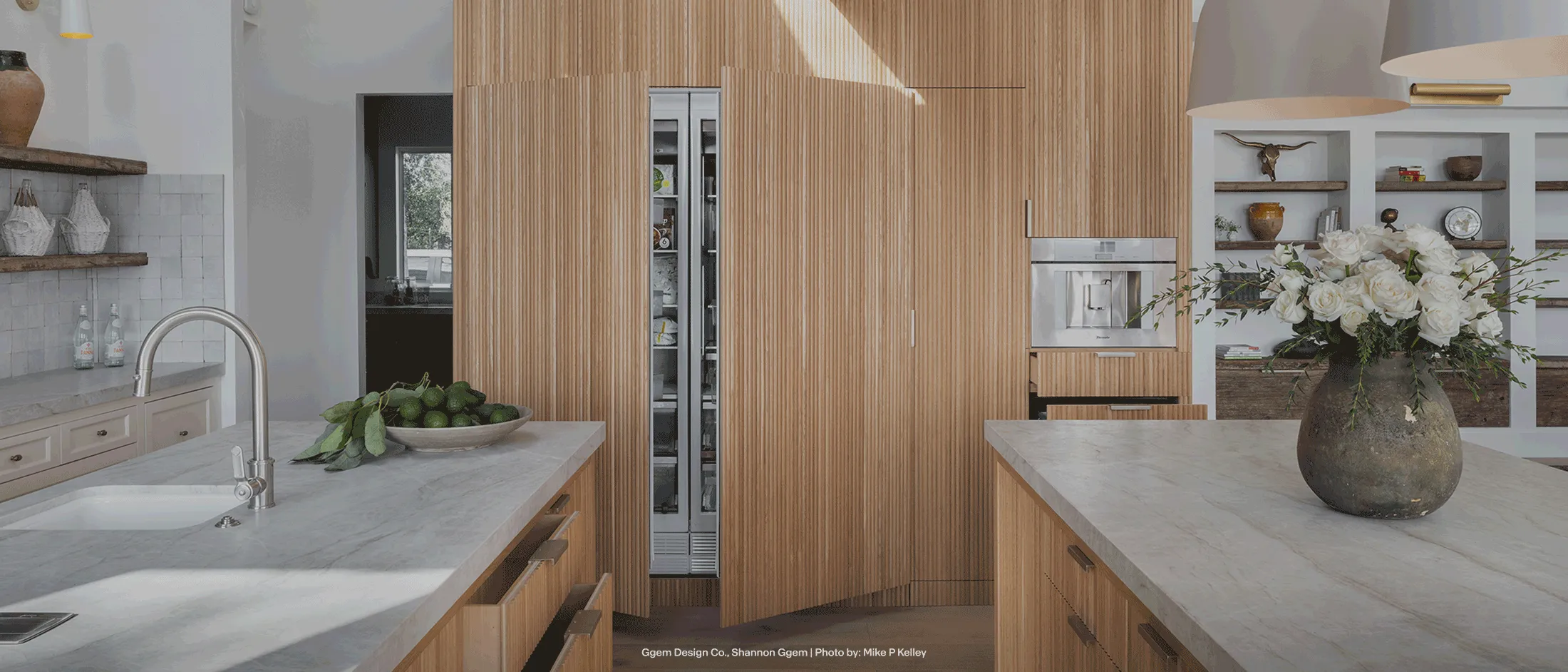 Thermador modern kitchen with wood-paneled cabinets, open drawers, a marble countertop, a bowl of avocados, and a partially open refrigerator.