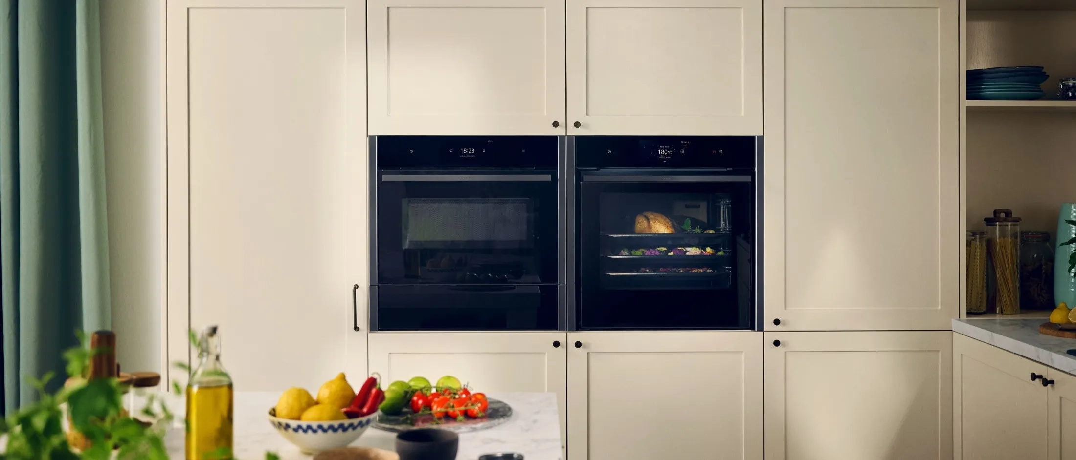Light kitchen with colourful food on countertop and two NEFF built in cooking appliances in cabinet