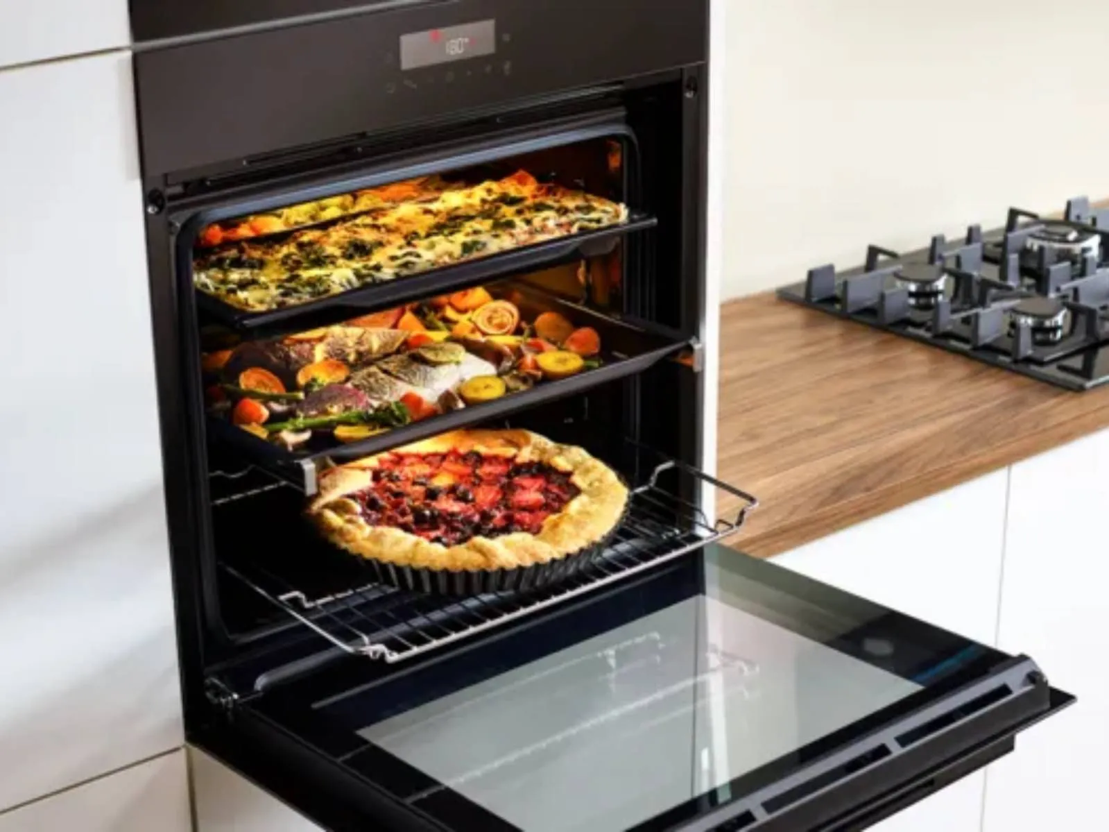 A modern oven holds roasted vegetables and a berry pie, set against a stylish kitchen with a warm wooden countertop.