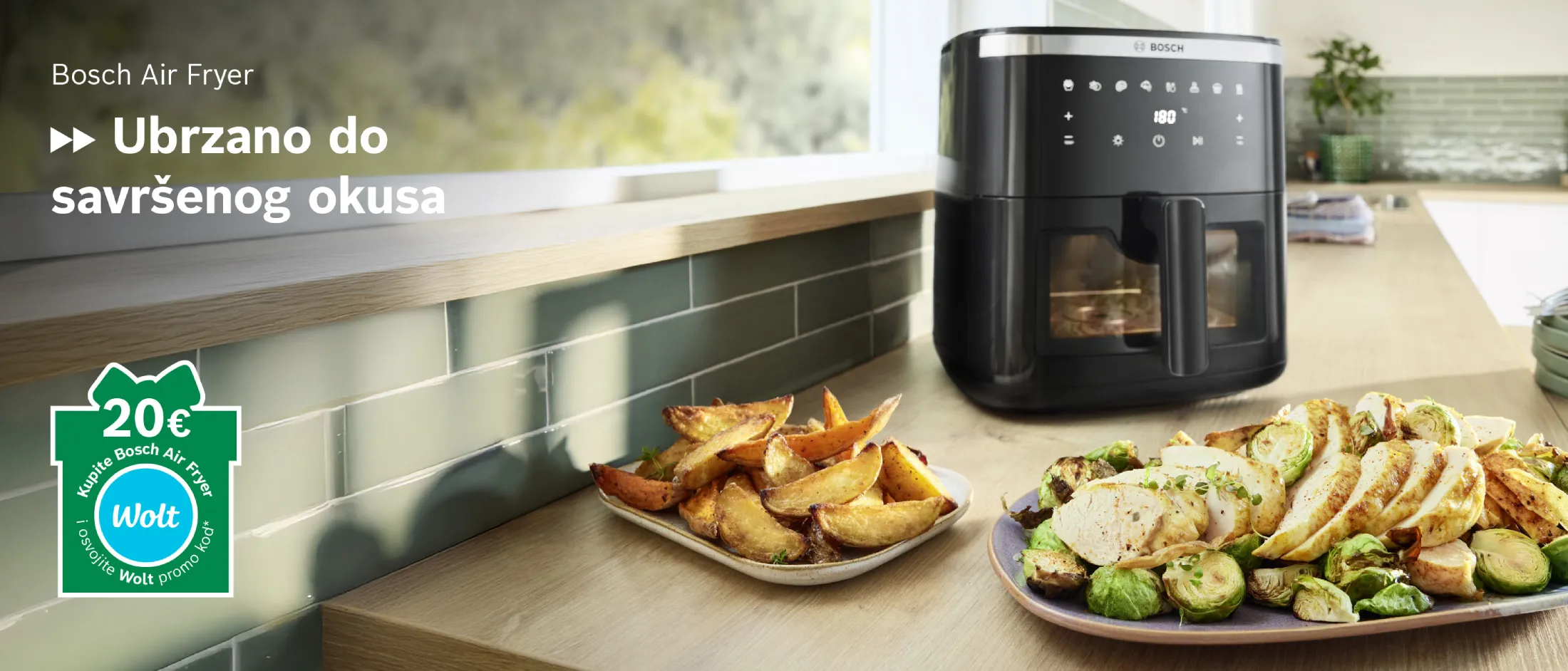Air fryer na kuhinjskoj radnoj ploči s tanjurima kuhane hrane, uključujući pomfrit i povrće