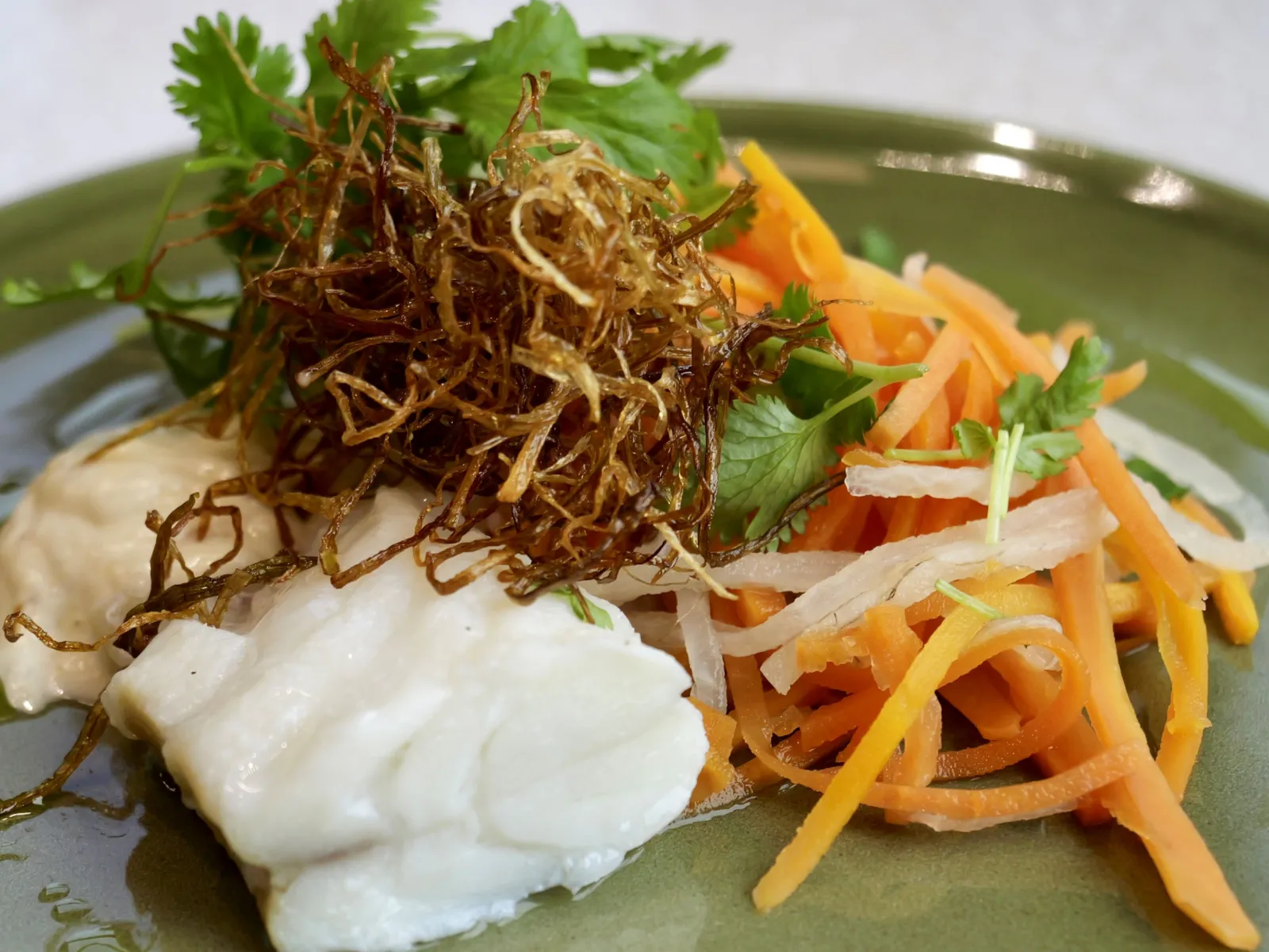 Tallerken med kokt fisk, strimlede gulrøtter, grønt og sprøstekt garnityr.